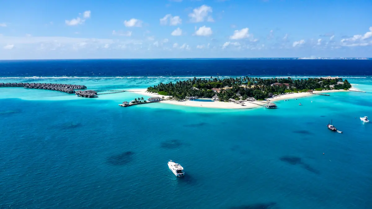 Aerial view of a Maldivian island with white sand, palms and overwater villas in a turquoise lagoon
