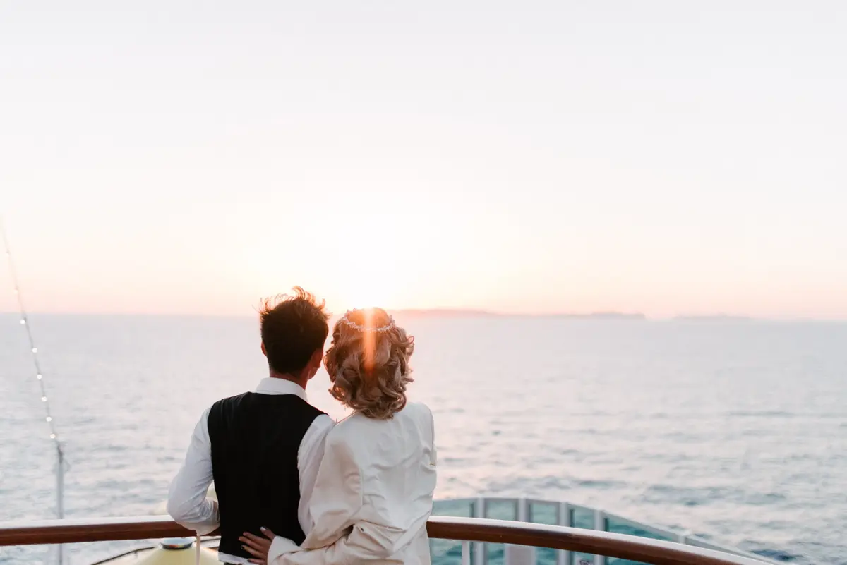 A couple on a cruise ship deck watching the sun set over the sea