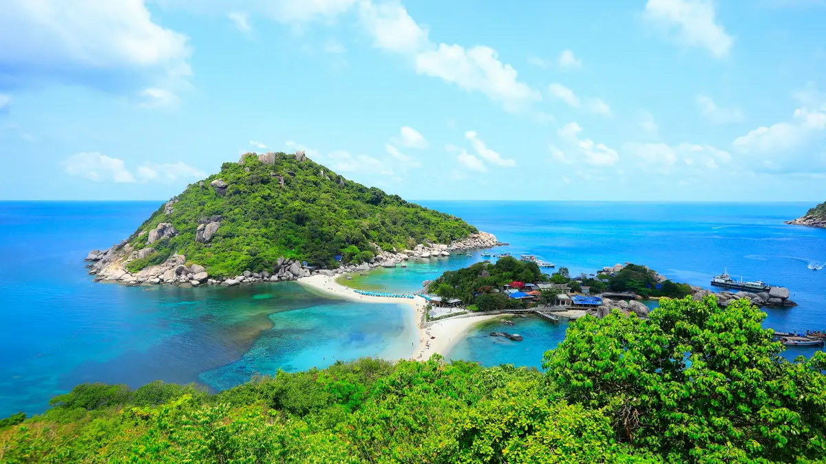 A green island with a sandy spit and turquoise water under a bright sky in Thailand