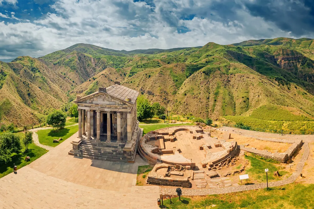 Luftaufnahme des Tempels von Garni mit seinen Ruinen am Rand einer grünen Schlucht unter bewölktem Himmel