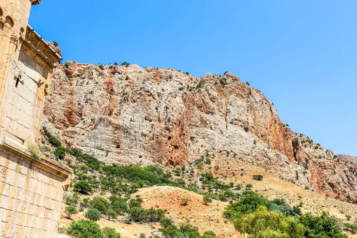 Rote und ockerfarbene Felswände der Noravank-Schlucht über der Steinmauer des Klosters unter klarem blauem Himmel