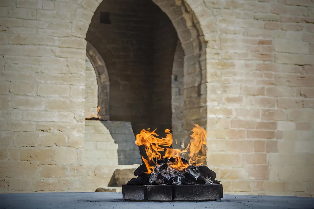 Eine Flamme brennt in einem steinernen Feueraltar unter alten Bogenmauern