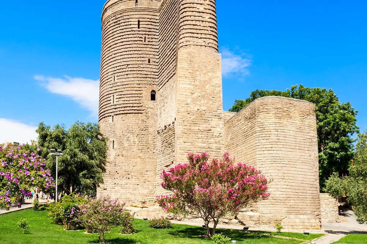 Der Jungfrauenturm in der Altstadt von Baku, davor blühende Bäume und eine Wiese