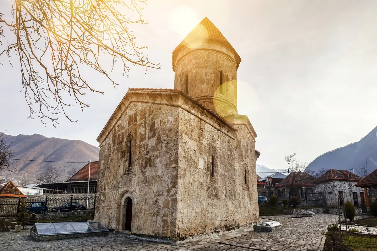 Une petite église en pierre à tour conique dans une vallée de montagne, éclairée par le soleil bas
