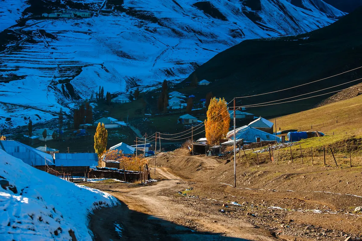 Ein leicht verschneites Bergdorf mit Feldweg und goldener Pappel im Abendlicht