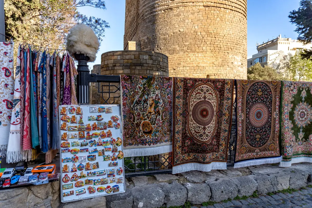 Tapis, foulards et magnets souvenirs exposés près d’une vieille tour en pierre