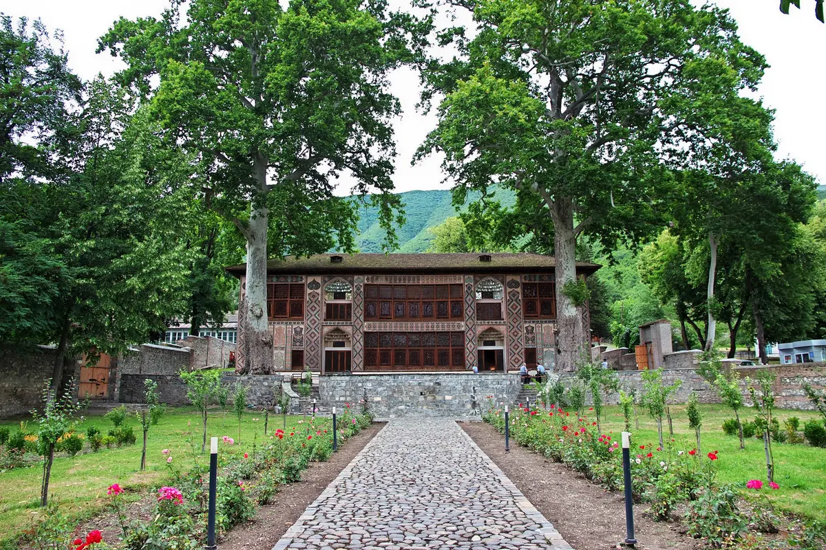 Der Khanspalast von Scheki mit geschnitzter Holzfassade, umgeben von hohen Platanen und einem Rosenweg