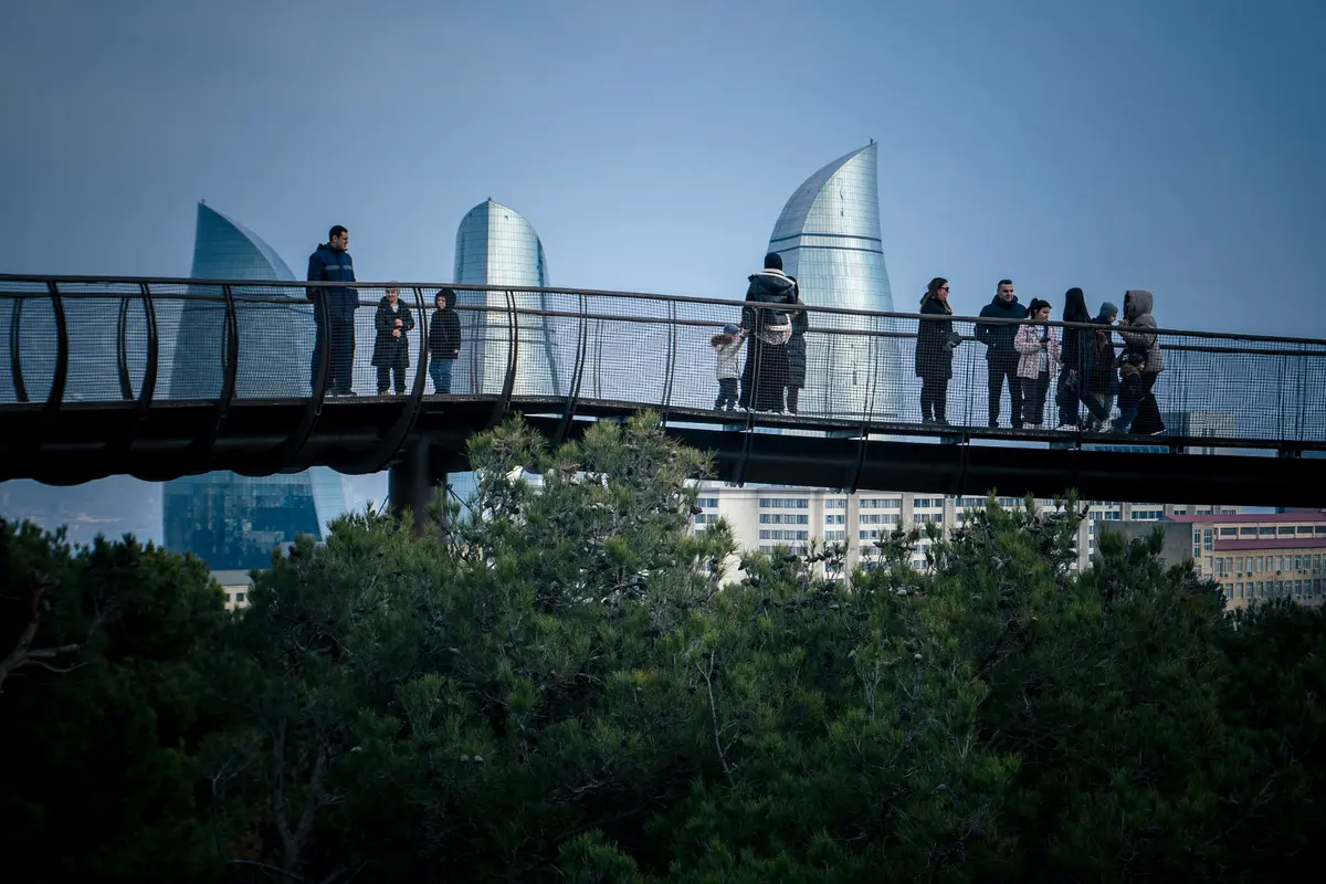 Besucher auf einer Fußgängerbrücke, dahinter die Flame Towers von Baku