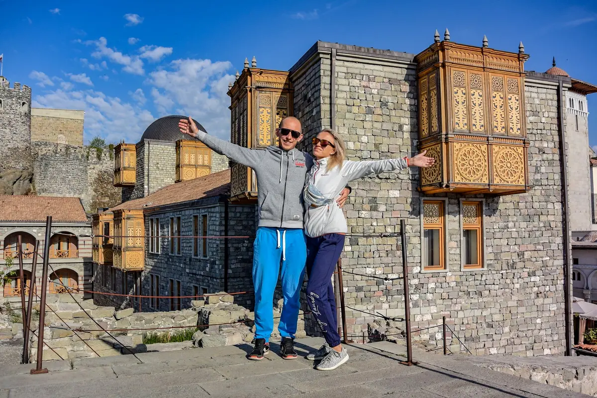 Ein Paar mit ausgebreiteten Armen auf der Festung Rabati in Achalziche, dahinter geschnitzte Holzbalkone