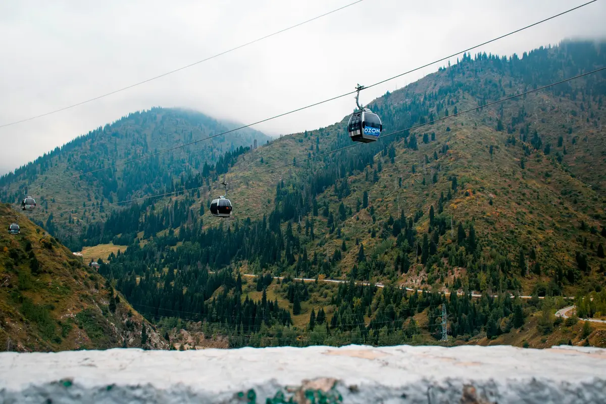 Cabinas del teleférico ascendiendo sobre laderas boscosas sobre Medeu, Almaty