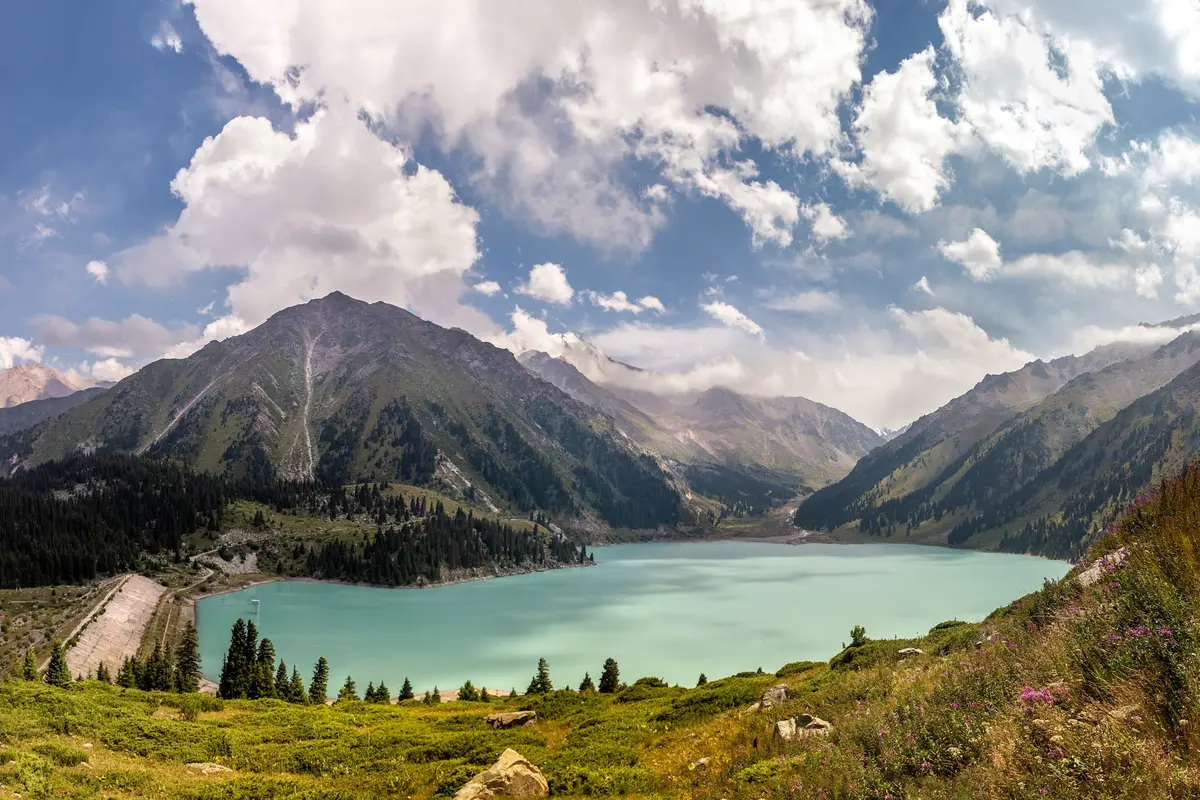 Der türkisfarbene Große Almaty-See, umgeben von Bergen und dramatischen Wolken