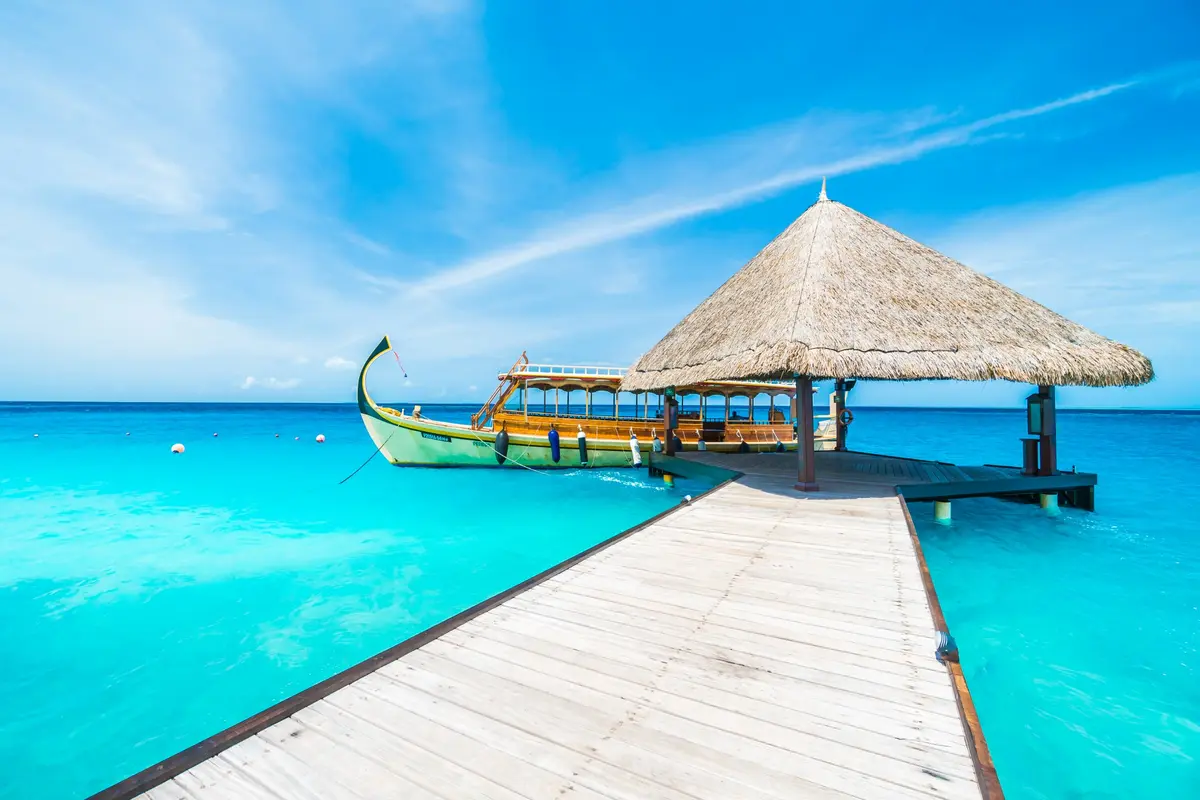 Un dhoni traditionnel à un ponton au toit de chaume au-dessus des eaux des Maldives