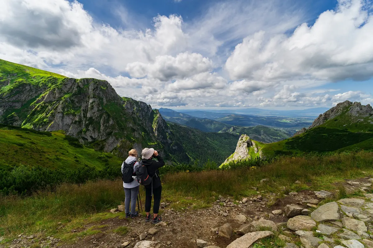 Zwei Wanderer blicken über ein grünes Tatra-Tal unter wolkigem Himmel