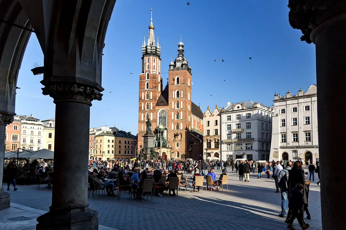 Die Marienkirche, gesehen durch die Arkaden der Tuchhallen, mit Café-Tischen und Menschen auf dem Krakauer Hauptmarkt