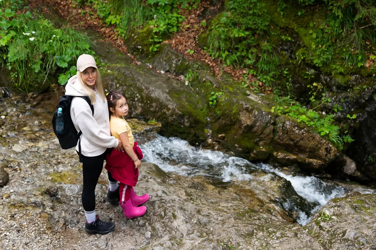 Eine Mutter und ihre kleine Tochter in Wanderkleidung an einem Bergbach auf einem Waldweg in der Tatra