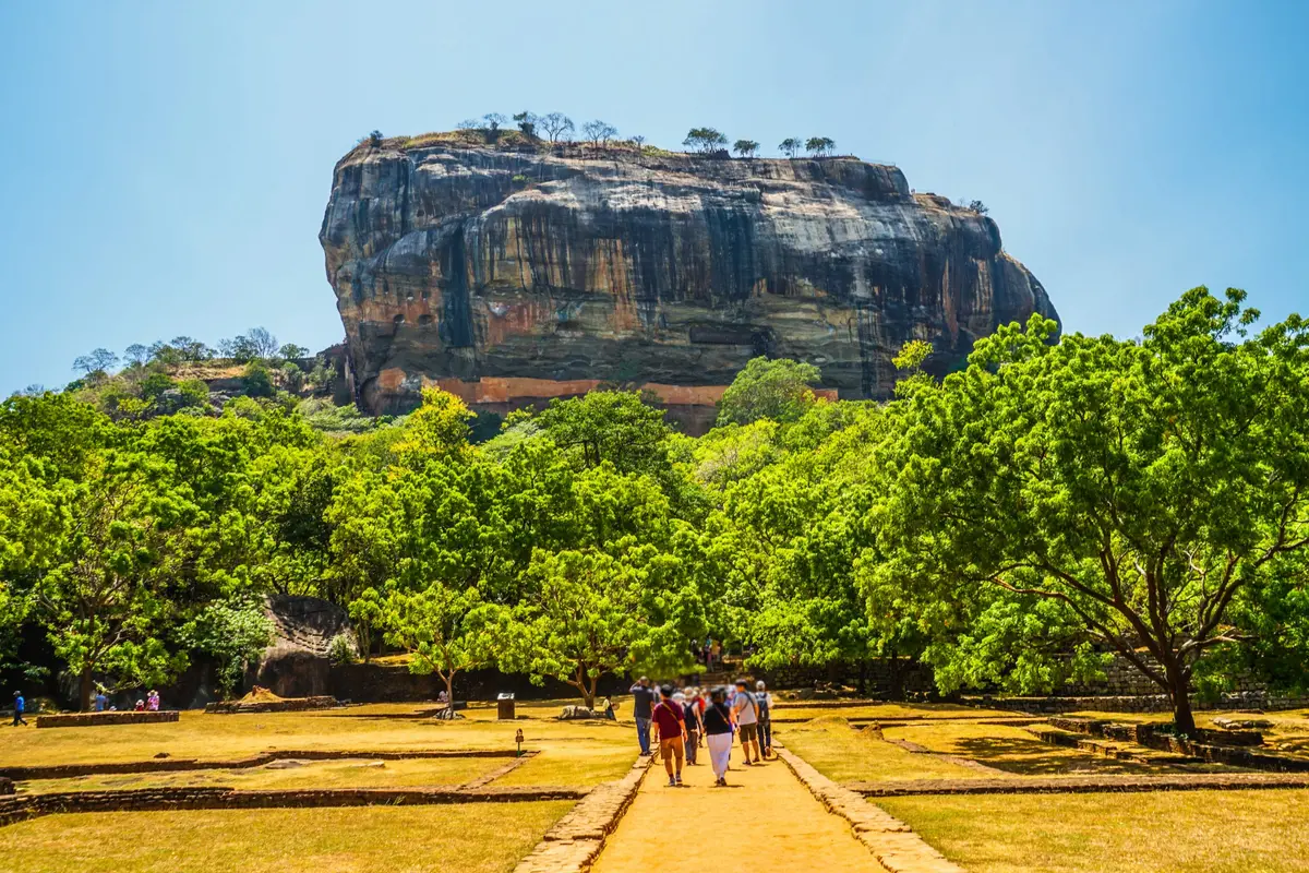 Besucher gehen auf dem Weg zum gewaltigen Sigiriya-Felsen zwischen grünen Bäumen in Sri Lanka