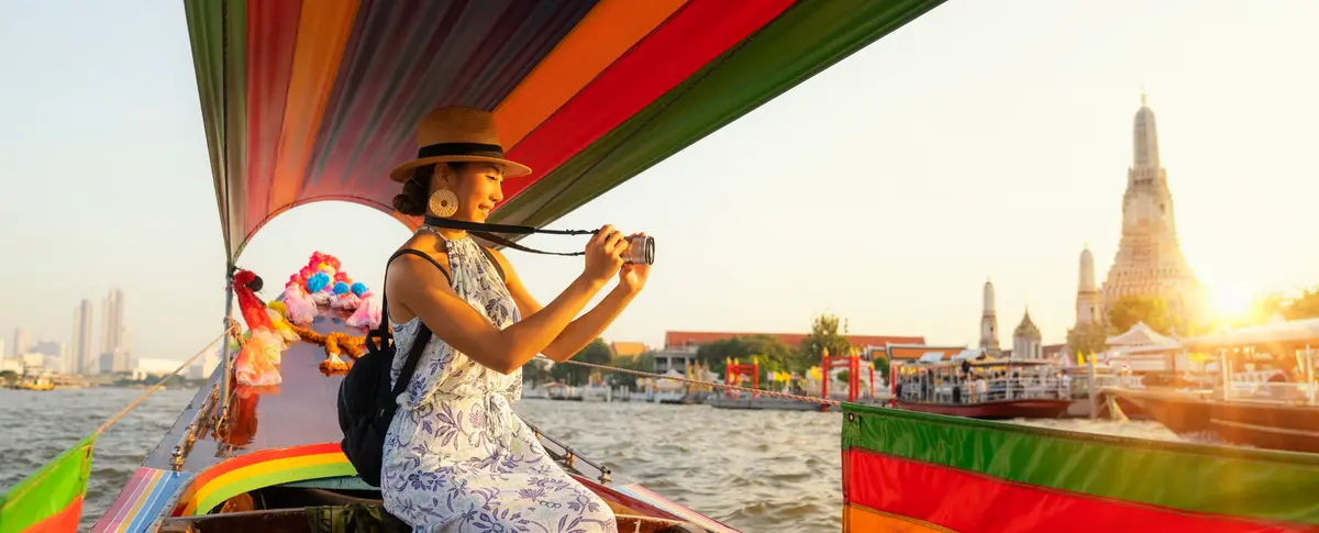 Eine Reisende fotografiert bei Sonnenuntergang Wat Arun von einem bunten Longtailboot auf dem Chao Phraya