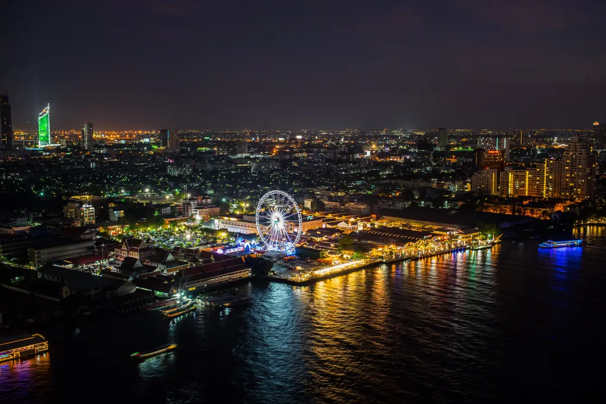 Nächtlicher Blick von oben auf das beleuchtete Riesenrad und den Uferbasar Asiatique am Chao Phraya in Bangkok