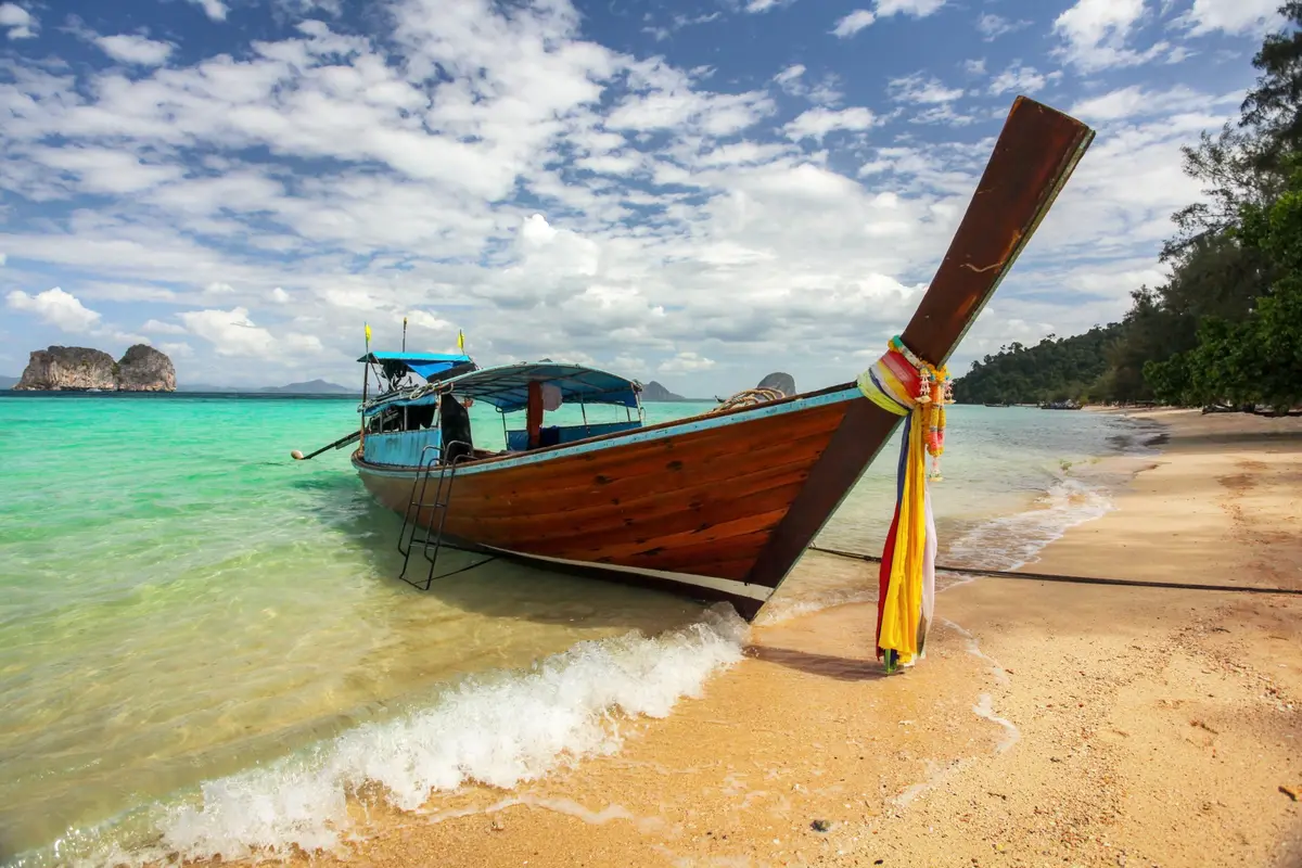 Ein hölzernes Longtailboot an einem Sandstrand mit türkisem Wasser in der Region Krabi