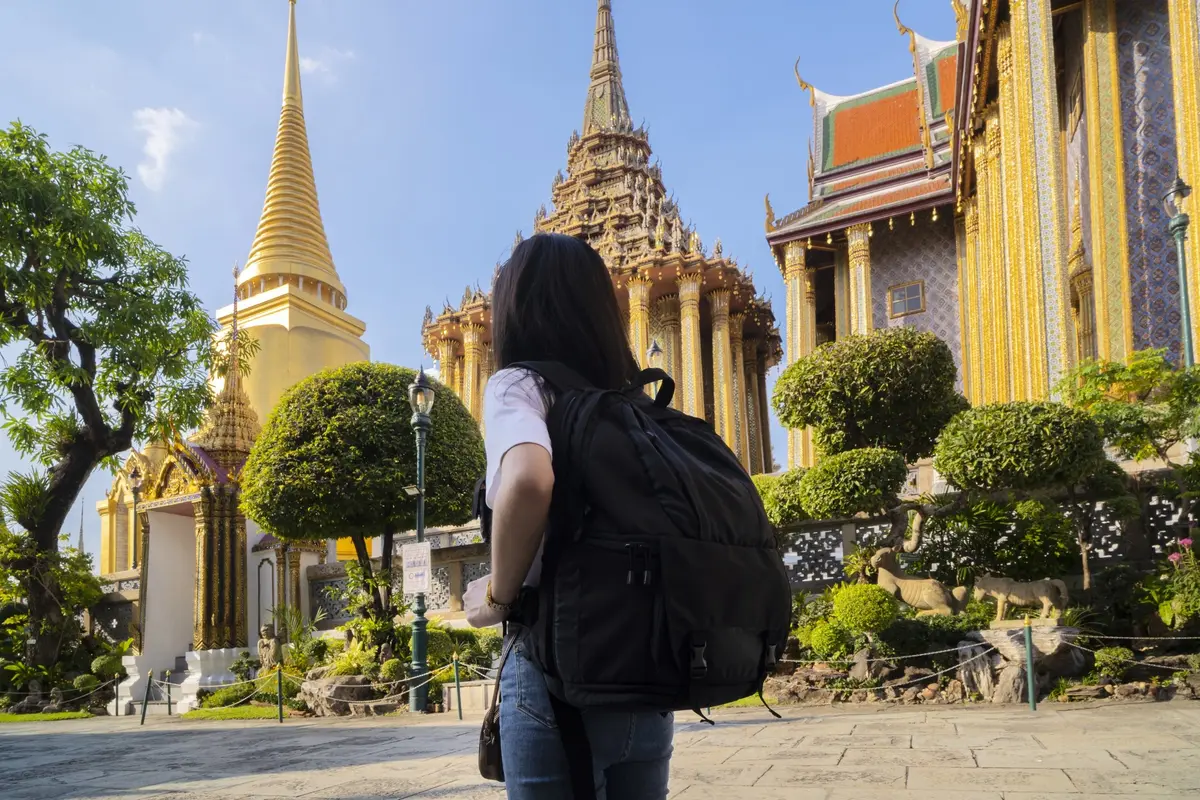 Eine Reisende mit Rucksack vor den Tempeln des Großen Palastes in Bangkok