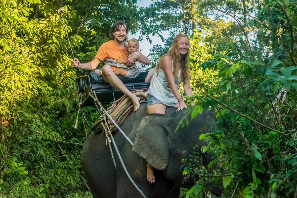 Eine glückliche Familie mit Kleinkind reitet auf einem Elefanten durch grünen tropischen Wald