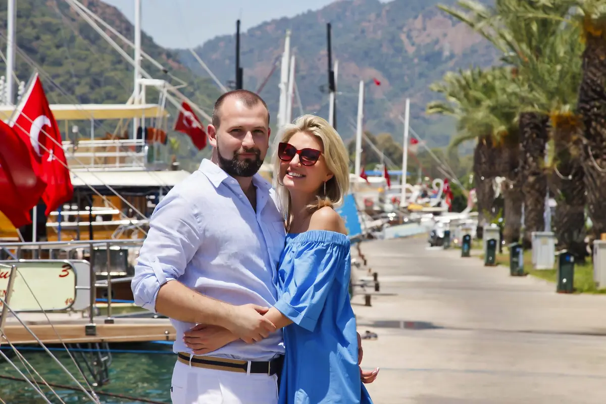 Ein Paar umarmt sich auf einer Yachthafen-Promenade mit Yachten und türkischen Flaggen