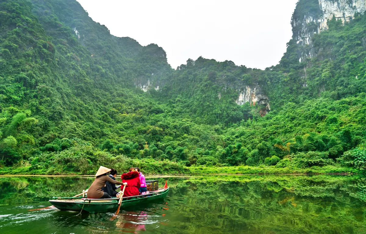 Ein Ruderboot zwischen grünen Kalksteinhügeln bei Trang An, Ninh Binh