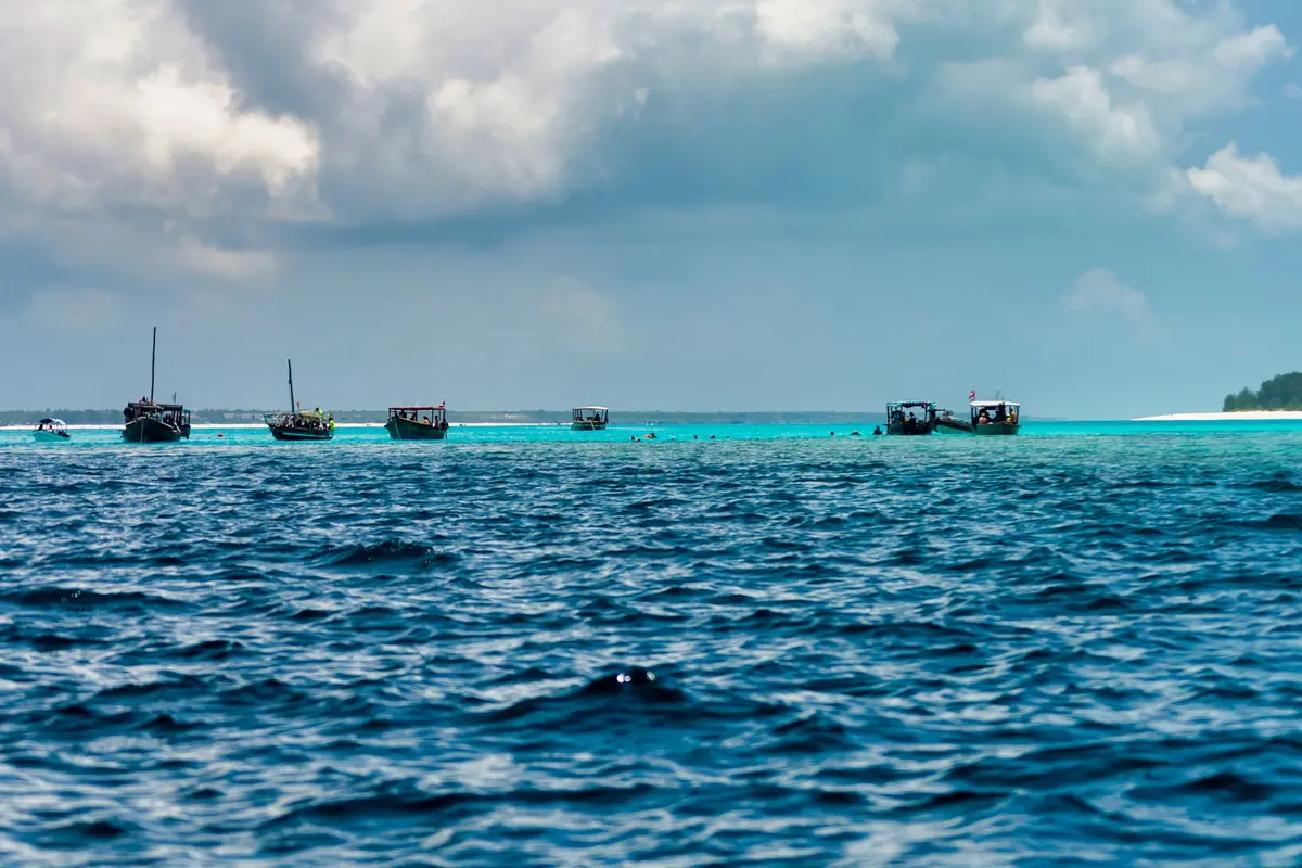 Ausflugsboote und Schnorchler auf türkisfarbenem Wasser vor der Insel Mnemba, Sansibar