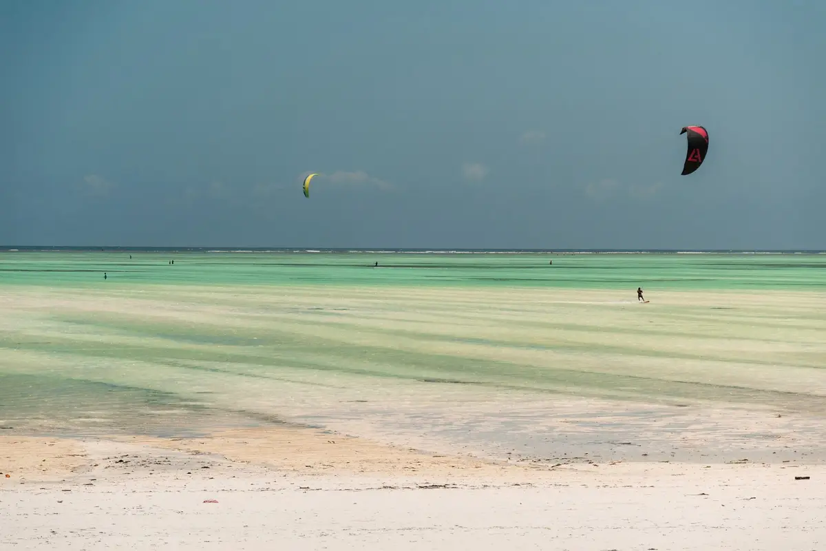 Kitesurfer auf der flachen grünen Lagune des Paje-Strandes bei Ebbe, im Vordergrund weißer Sand