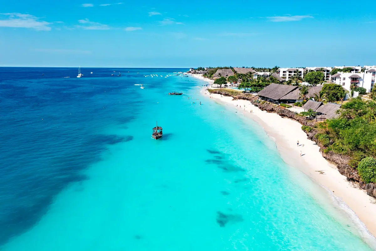 Luftaufnahme des türkisfarbenen Strandes von Nungwi auf Sansibar mit Holz-Dhau, weißem Sand und reetgedeckten Strandhotels