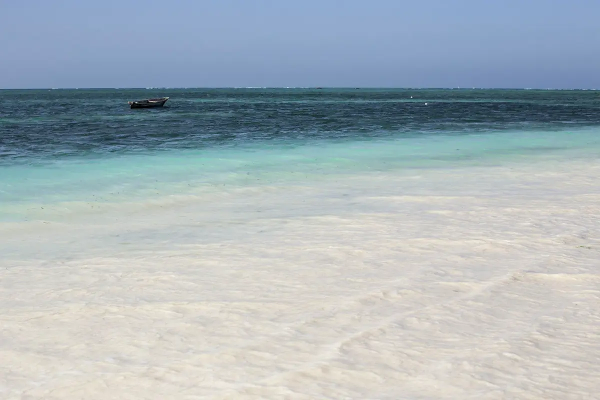 Ein kleines Holzboot auf türkisfarbenem Wasser hinter einem weißen Sandstrand auf Sansibar