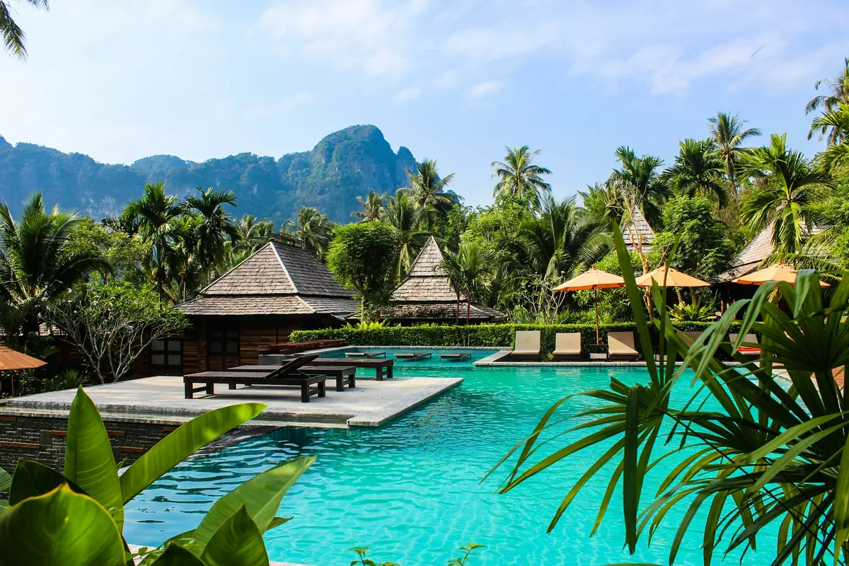 Tropical resort with a turquoise pool and wooden pavilions below green mountains