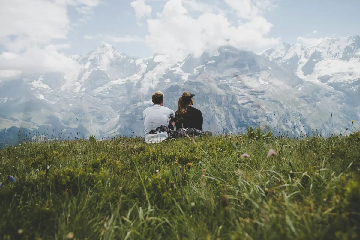 A couple sitting on the grass facing the mountains